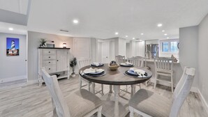 A dining area with a round table, white chairs, and a white cabinet with drawers. - Pier Point South Ocean View Condo D-44 (St. Augustine)