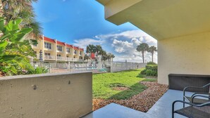 A balcony with a view of a pool, a grassy area, and a row of buildings with red roofs. - Pier Point South Ocean View Condo D-44 (St. Augustine)