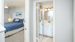 Een slaapkamer met een bed, nachtkastje, plafondventilator en een spiegel aan de muur.