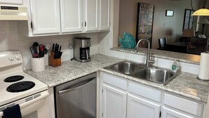 Una cocina moderna con armarios blancos, un lavamanos de acero inoxidable, una cafetera y un escurreplatos.