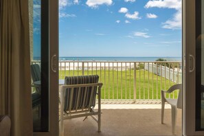 Ein Balkon mit Blick auf den Strand, eine Rasenfläche und ein weißer Zaun.