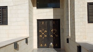 Une entrée d’immeuble avec une porte noire ornée de motifs décoratifs dorés, un sol carrelé et un mur en pierre.