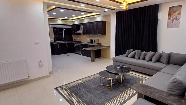 Un salon moderne avec un canapé gris, deux tables basses rondes et un tapis noir et doré.