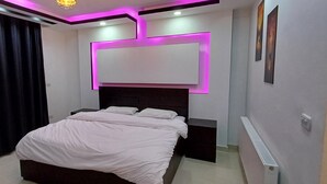 Une chambre à coucher moderne, équipée d’un lit, de tables de chevet, d’un téléviseur fixé au mur et d’un luminaire suspendu au plafond.