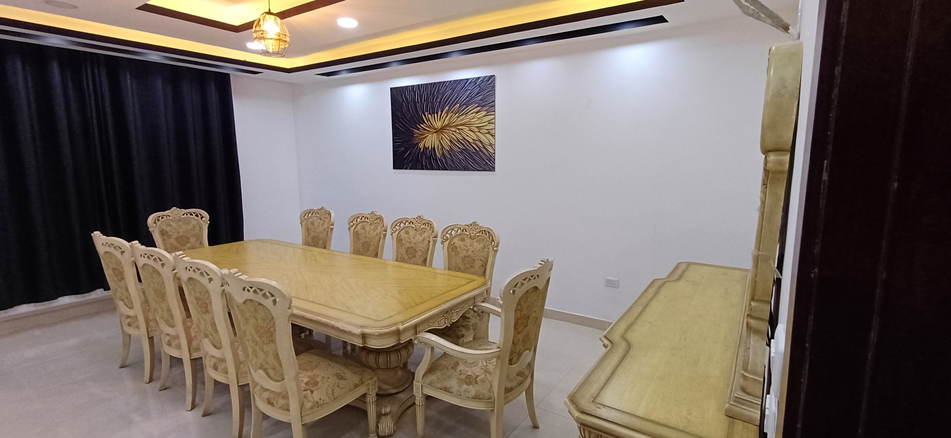 Un salón de conferencias con una mesa de madera y sillas estampadas con motivos florales, un cuadro abstracto en blanco y negro en la pared, y una lámpara en el techo.