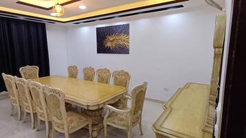 Un salón de conferencias con una mesa de madera y sillas estampadas con motivos florales, un cuadro abstracto en blanco y negro en la pared, y una lámpara en el techo.