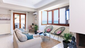 A modern living room with a sofa, a coffee table, and chairs. There is a view of the sea through large windows. - Nova Sea View Apartment Seafront (Kokkini Hani)