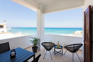 En balkon med udsigt over havet, et bord med stole og en potteplante.