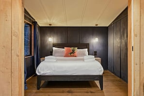 A bedroom with a dark wood bed, white bedding, and a single decorative pillow.