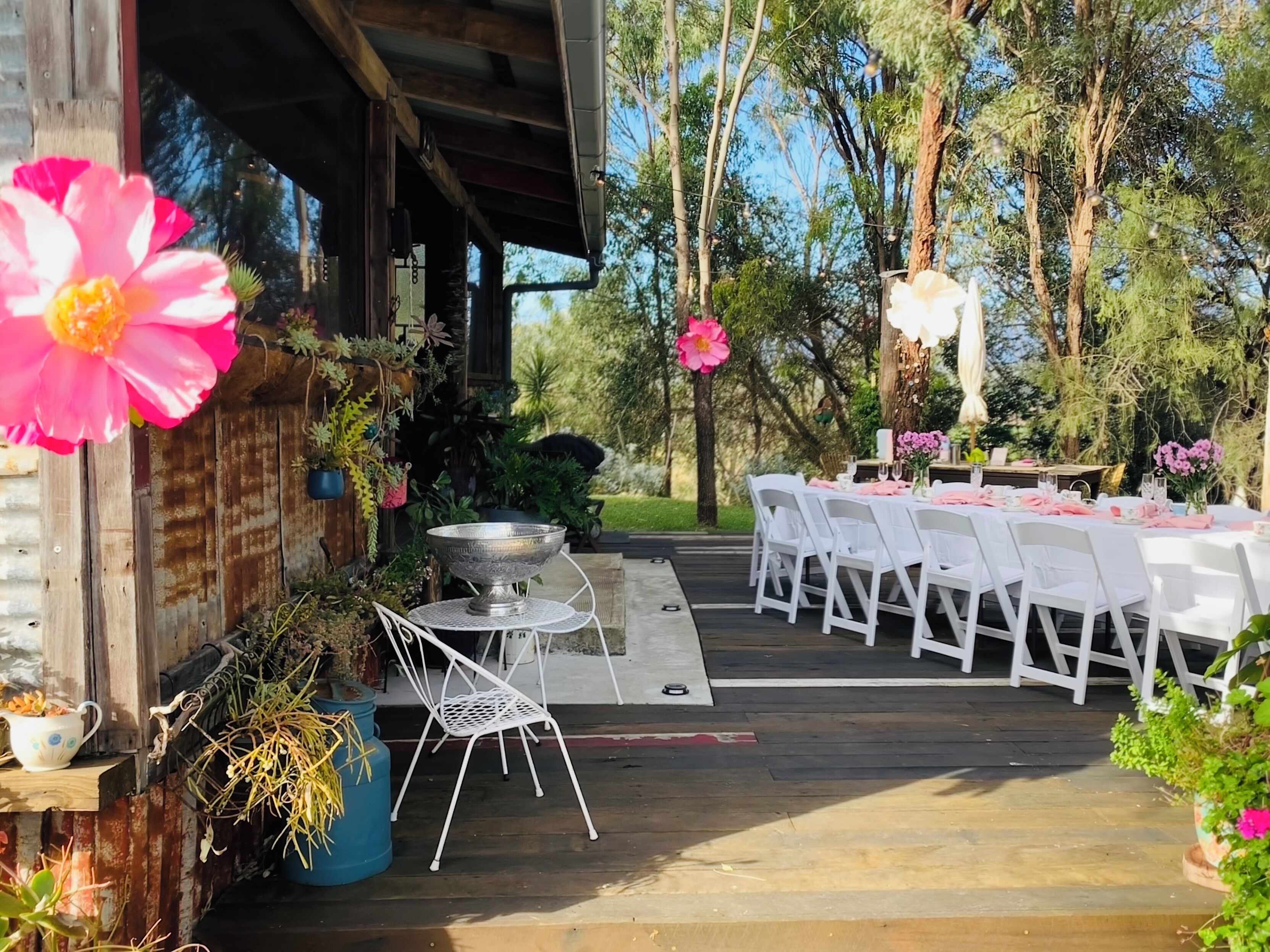 Un espace extérieur aménagé pour les repas, avec des tables et des chaises blanches, entouré de plantes et de fleurs en pot.