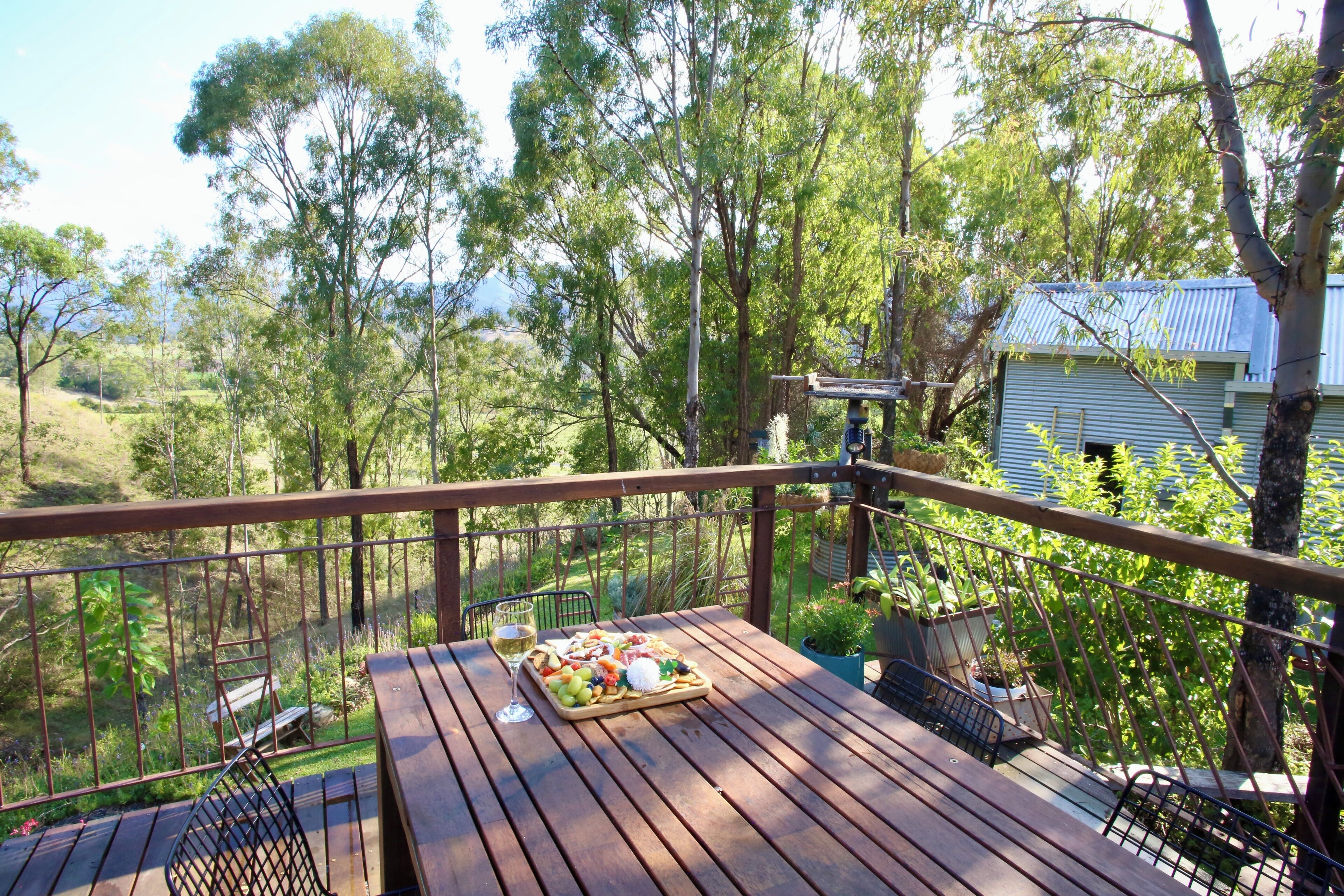 A wooden deck with a table set for a meal, surrounded by trees and a house in the background.