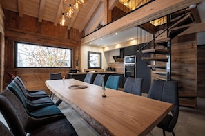 Eine moderne Küche mit Holzvertäfelung, ein Essbereich mit einem langen Tisch und Stühlen sowie eine Treppe, die in ein Obergeschoss führt.