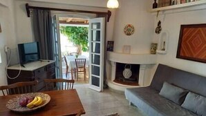 En stue med sofa, spisebord med frugt, fjernsyn og pejs.