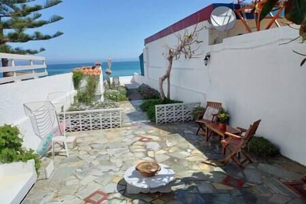 A patio with stone flooring, a table with chairs, and a view of the sea.