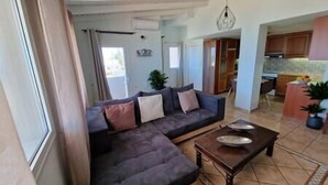 Ein Wohnzimmer mit einem dunkelgrauen Sofa, einem Holztisch und Blick in einen Küchenbereich.
