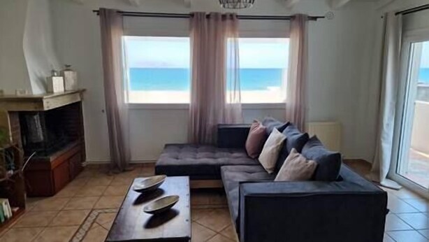 Ein Wohnzimmer mit einem dunkelgrauen Sofa, einem kleinen Tisch mit Schalen und Meerblick durch große Fenster.