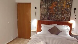 Ein Hotelzimmer mit einem Bett, einer Holztür, einer Wand mit einem Gemälde und zwei Wandleuchten.