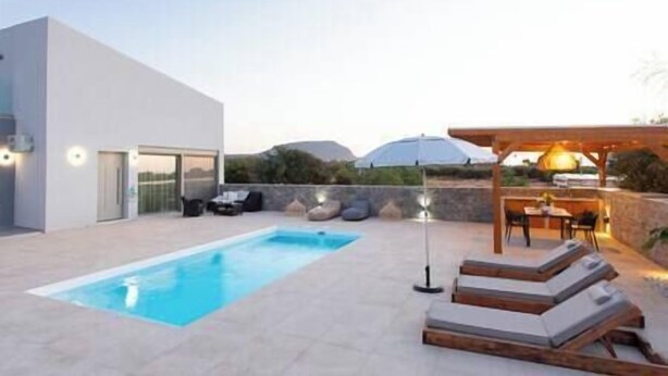 A modern outdoor pool area with a clear blue pool, lounge chairs, and a pergola with a table and chairs.