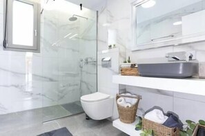 Een moderne badkamer met een glazen douchecabine, een wit toilet, een grote spiegel en een wastafelmeubel met een grijze wasbak.