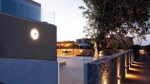 A modern building with a pool area, outdoor seating, and a tree-lined pathway.