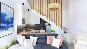 A modern living room with a dark sofa, a staircase with wooden railings, and a hanging light fixture.