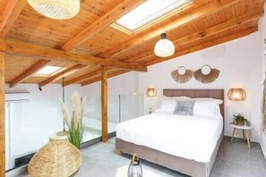 Een slaapkamer met een houten plafond, een groot bed, twee wandlampen en een dakraam.