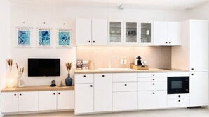 A modern kitchen with white cabinetry, a flat-screen TV, and decorative wall art.
