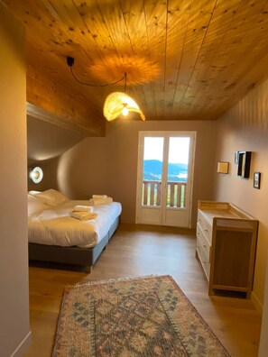 A bedroom with a bed, a dresser, a rug, and a view through a door. - LE PERCHOIR - 14 guests - Lake view - Sauna, Gérardmer (Gérardmer)