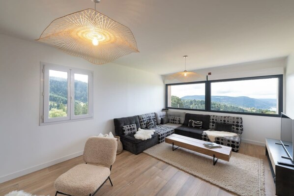A modern living room with a sofa set, a chair, a coffee table, and a large window offering a view of the outdoors.