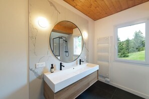 A modern bathroom with a marble wall, a wooden vanity, a large mirror, and a window with a view of greenery. - LE PERCHOIR - 14 guests - Lake view - Sauna, Gérardmer (Gérardmer)