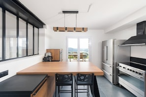 A modern kitchen with a central island, black chairs, and a stainless steel oven. - LE PERCHOIR - 14 guests - Lake view - Sauna, Gérardmer (Gérardmer)
