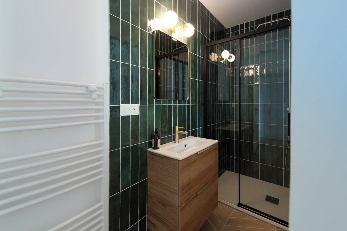 A modern bathroom with a wooden vanity, a glass shower enclosure, and a wall-mounted mirror with lights.