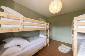 A bunk bed room with a wooden ladder, white bedding, and a hanging light fixture.