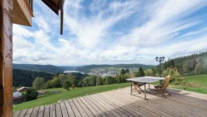 Um deck de madeira com mesa e cadeiras, com vista para um vale e um lago.