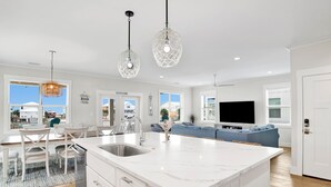 Una cocina moderna con isla de mármol blanco, pileta de acero inoxidable e iluminación colgante.