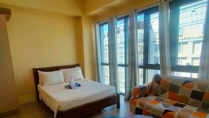 Una habitación de hotel con cama, sofá, una mesita y ventanas amplias con cortinas.