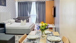 Una sala de estar moderna con comedor, sofá gris y televisor montado en la pared.