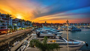 A marina with boats docked, a waterfront promenade, and buildings with balconies.