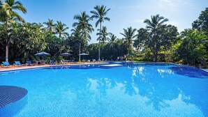 A clear blue pool surrounded by lounge chairs and umbrellas, with palm trees in the background.