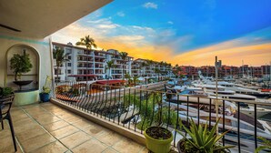 A balcony with potted plants, a view of a marina with boats, and a building with balconies.