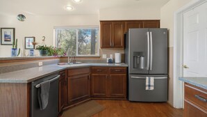 A kitchen with wooden cabinets, a stainless steel refrigerator, a sink, and a window with a view of trees. - Pine Cliff (Flagstaff)