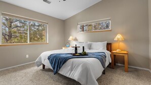 A bedroom with a bed, two bedside tables, a ceiling fan, large windows, and artwork on the wall. - Pine Cliff (Flagstaff)