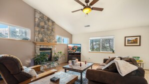 A cozy living room with a stone fireplace, wooden furniture, and a ceiling fan. - Pine Cliff (Flagstaff)
