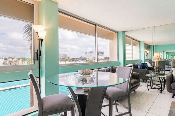A modern living room with a glass table, grey sofas, and a view of a swimming pool.