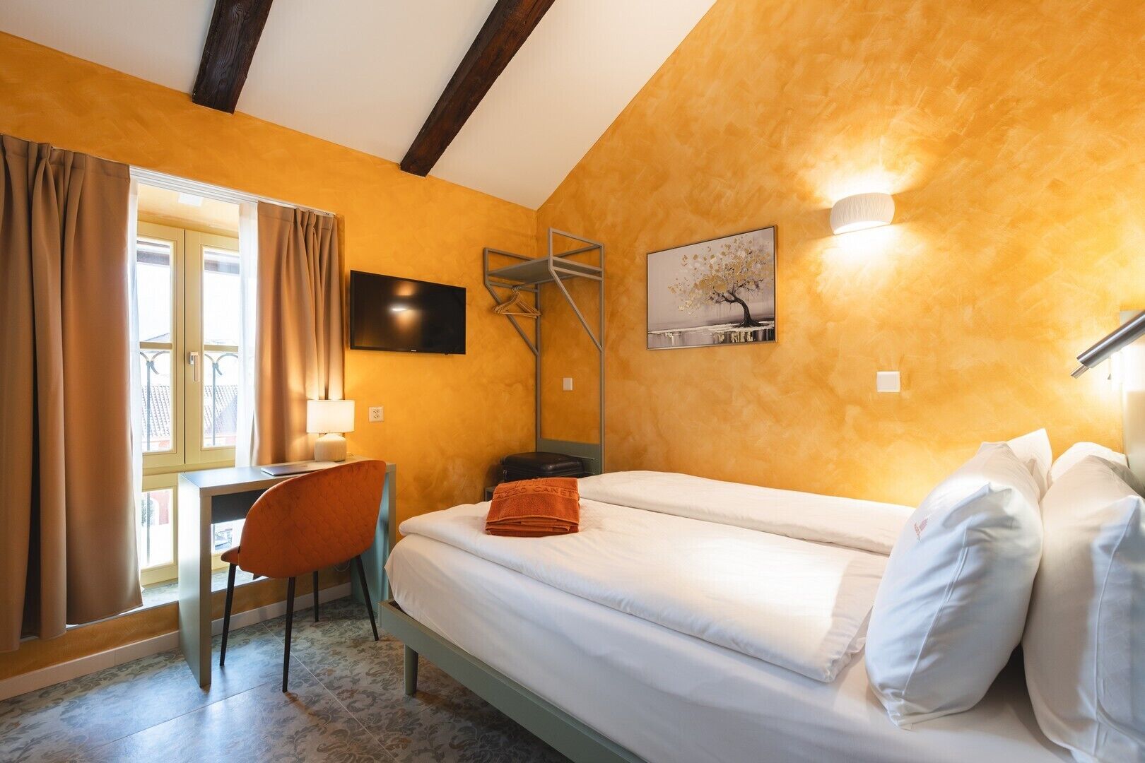 A hotel room with a bed, a desk, a chair, a TV, and a window with curtains.