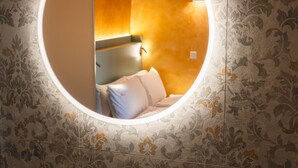A circular mirror with a bed and a wall with a floral pattern. - Palazzo Canetti Locarno (Locarno)