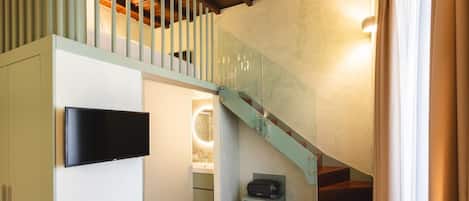 A modern interior with a staircase, a flat-screen TV, and a small seating area.