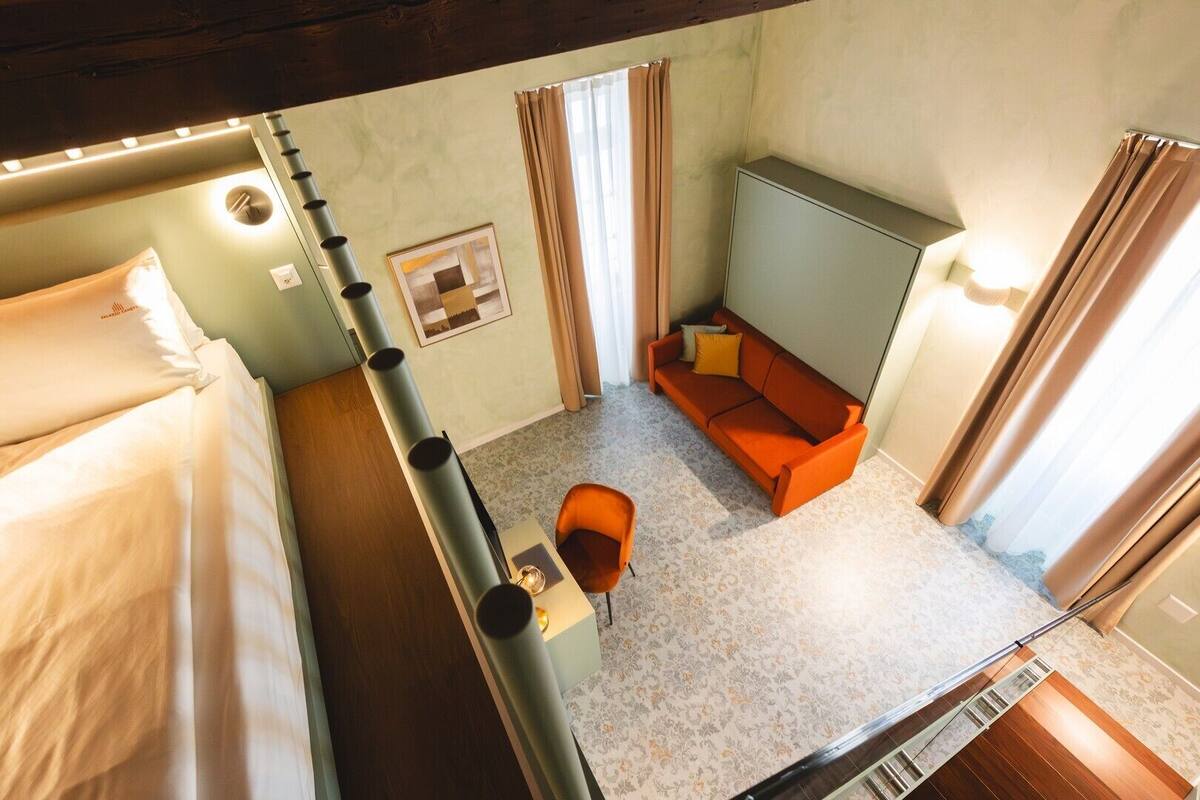 A compact hotel room with a bunk bed, a sofa, a small table, and a chair.