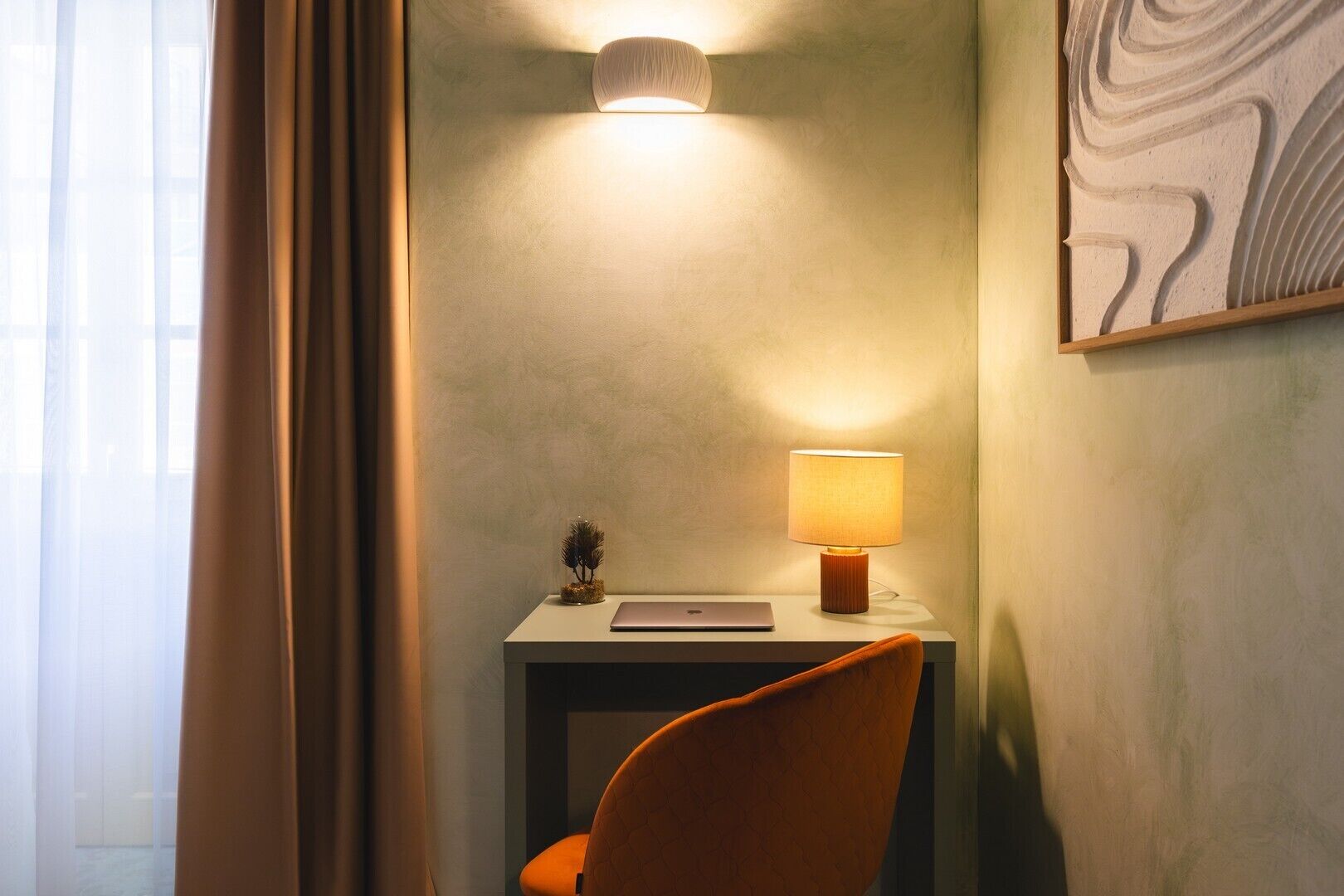 Une chambre d’hôtel avec un bureau, une lampe, une chaise et un tableau au mur.