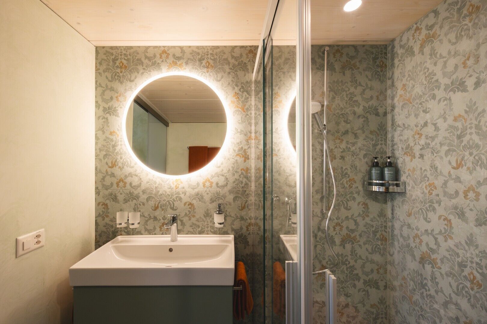 A bathroom with a round mirror, a sink, and a shower.
